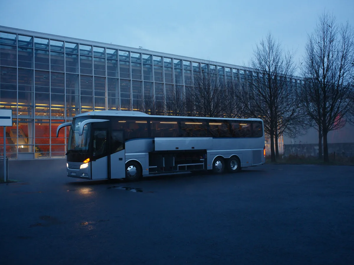 Reisebus vor einem beleuchteten Messegelände in der blauen Stunde